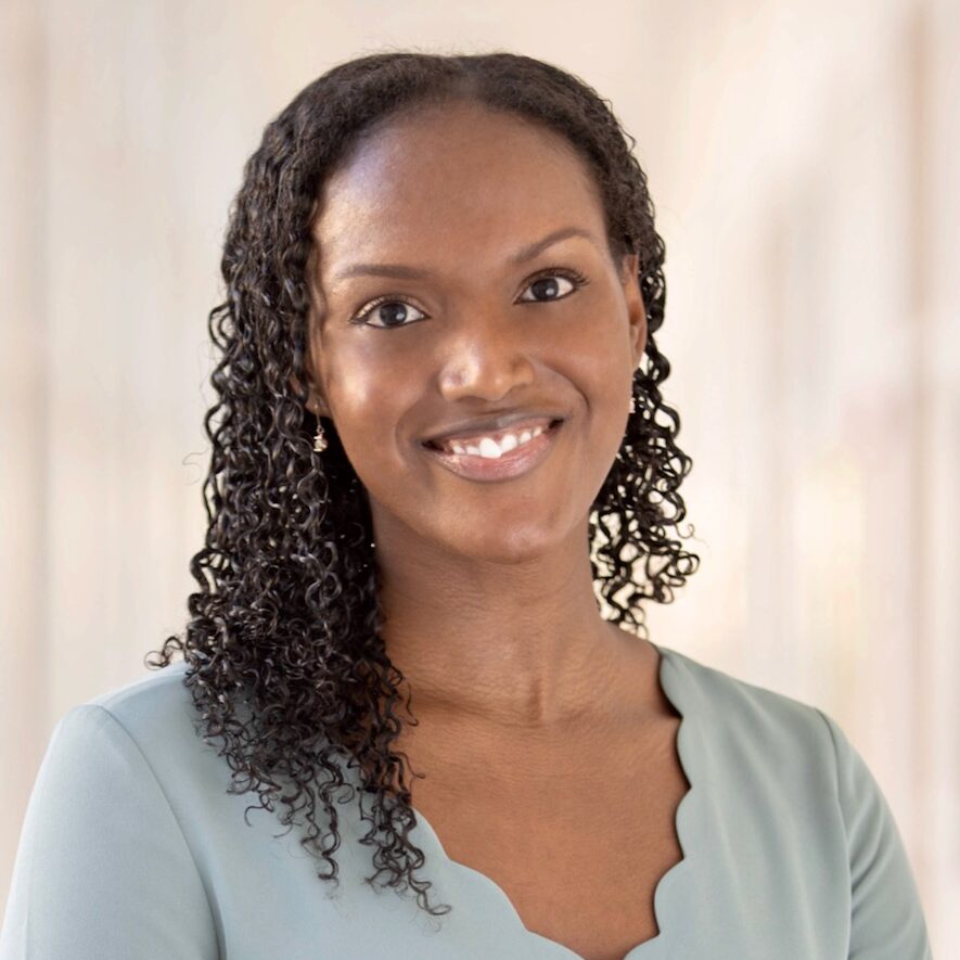 Leah is a young woman with dark brown curly hair. She is smiling at the camera.